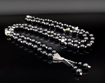 May include: A black beaded necklace with silver-coloured accents and a decorative pendant. The beads are round and glossy, reflecting light. The necklace is displayed on a black surface. The text "SJA SEM Jewelry ART" is visible.