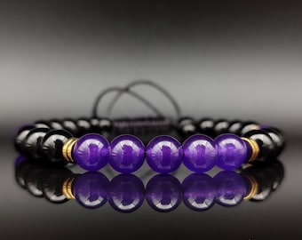 May include: A bracelet with alternating black and purple beads. The bracelet has a sliding knot closure and gold-coloured accents. The beads are round and polished, reflecting light. The bracelet is displayed on a reflective surface.