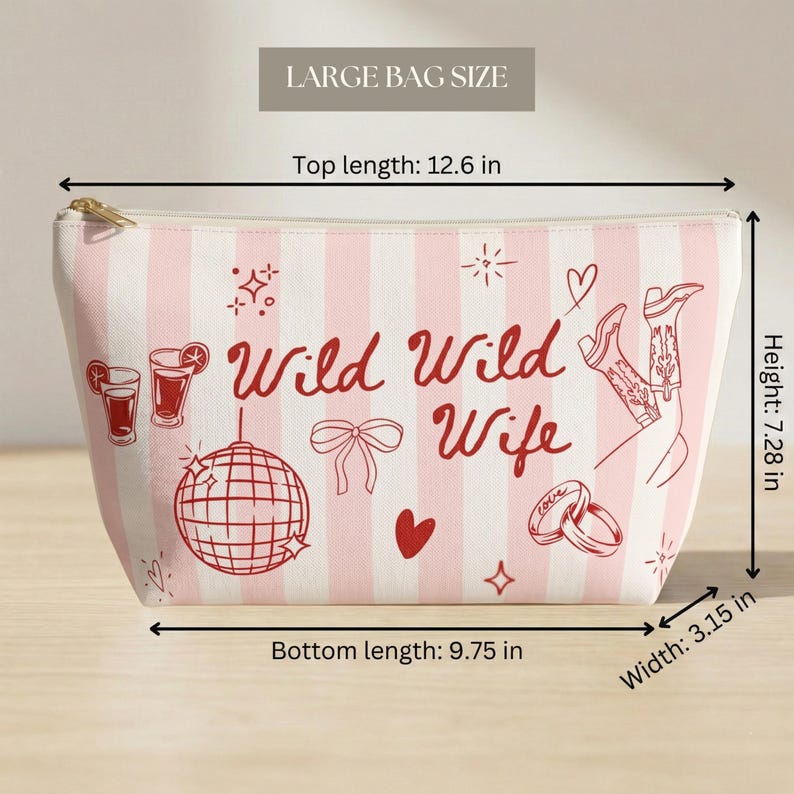 May include: A large, pink and white striped cosmetic bag with the text "Wild Wild Wife" in red. The bag features illustrations of cocktails, a disco ball, a bow, a heart, cowboy boots, and wedding rings. Top length is 12.6 inches.