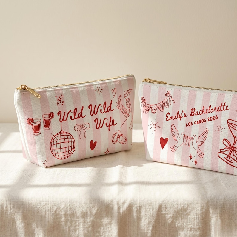 May include: Two rectangular cosmetic bags with pink and white stripes. One bag has the text "Wild Wild Wife" and the other says "Emily's Bachelorette Los Cabos 2026". Both bags have gold zippers and red illustrations.