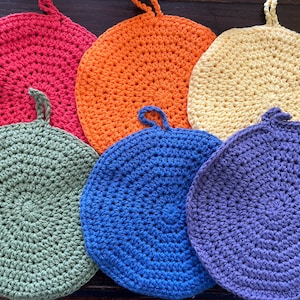 May include: Six crocheted pot holders in different colors, including red, orange, yellow, green, blue, and purple. The pot holders are round and have a textured surface.