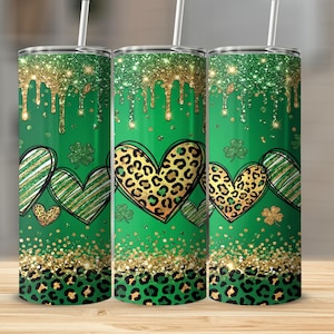 May include: Three green insulated tumblers with a St. Patrick's Day theme. Each tumbler features a gold glitter top, dripping design, and a pattern of hearts, shamrocks, and leopard print. The tumblers have white straws.