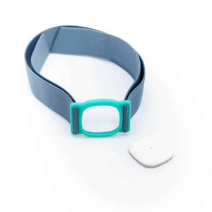 Pode incluir: Uma tira elástica azul com uma moldura retangular turquesa brilhante com cantos arredondados e um pequeno sensor quadrado branco separado com um ponto central. A tira está em forma de laço e o sensor está posicionado ao lado da moldura.