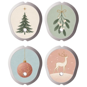 Könnte beinhalten: Vier kreisförmige Ornamente mit silbernen Rahmen und mittigen Löchern. Die Motive zeigen einen grünen Weihnachtsbaum auf Creme, Misteln auf Salbeigrün, eine rosa Kugel auf Hellblau und einen weißen Hirsch auf Altrosa mit Schnee.