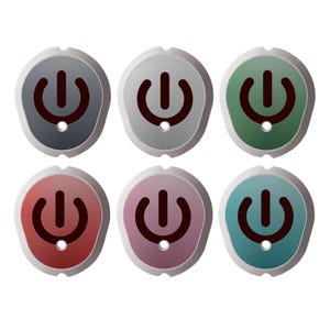 Puede incluir: Seis cubiertas para botones de encendido con forma de escudo redondeado, dispuestas en dos filas. Cada cubierta presenta un símbolo de encendido marrón oscuro y un pequeño orificio circular en la parte inferior. Los colores son gris oscuro, gris claro, verde, rojo, rosa y azul cerceta.