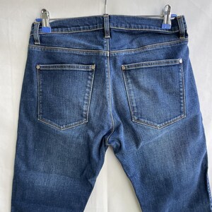 Puede incluir: Una taza de cer&aacute;mica blanca con un asa negra y el texto "But First, Coffee" en negrita negra. La taza se encuentra sobre un fondo borroso, sugiriendo un ambiente acogedor.