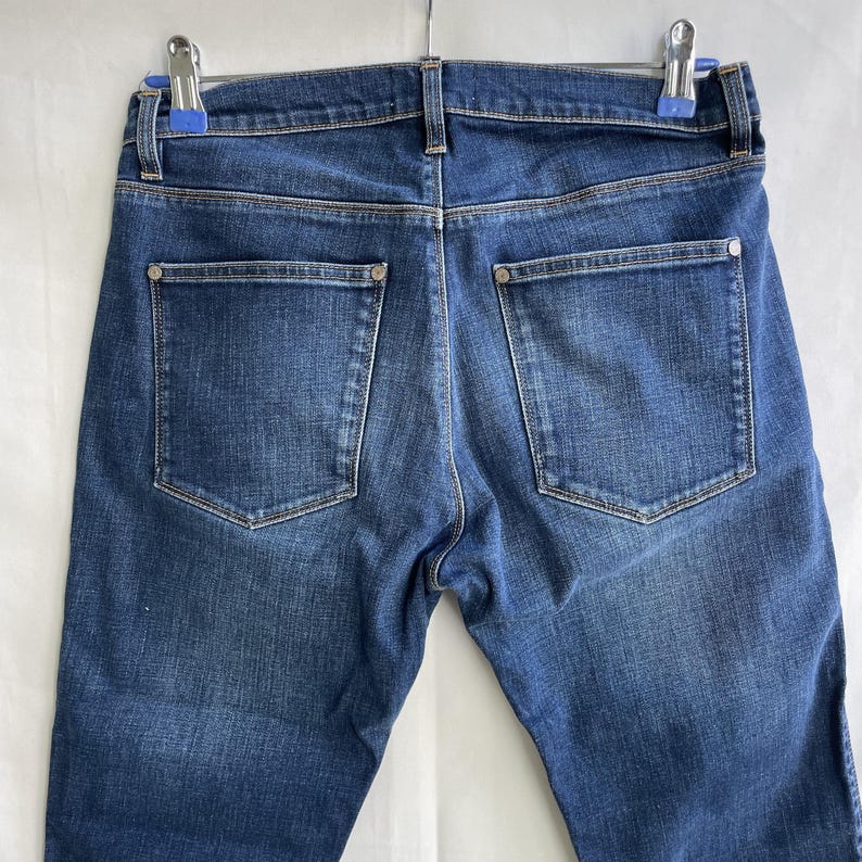 Puede incluir: Una taza de cer&aacute;mica blanca con un asa negra y el texto "But First, Coffee" en negrita negra. La taza se encuentra sobre un fondo borroso, sugiriendo un ambiente acogedor.