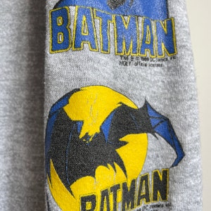 May include: Grey sweatshirt with a black and blue Batman logo and the text "TM & &copy; 1989 DC Comics Inc.  HGL, official licensee."  Below the logo is a yellow circle with a black bat silhouette.
