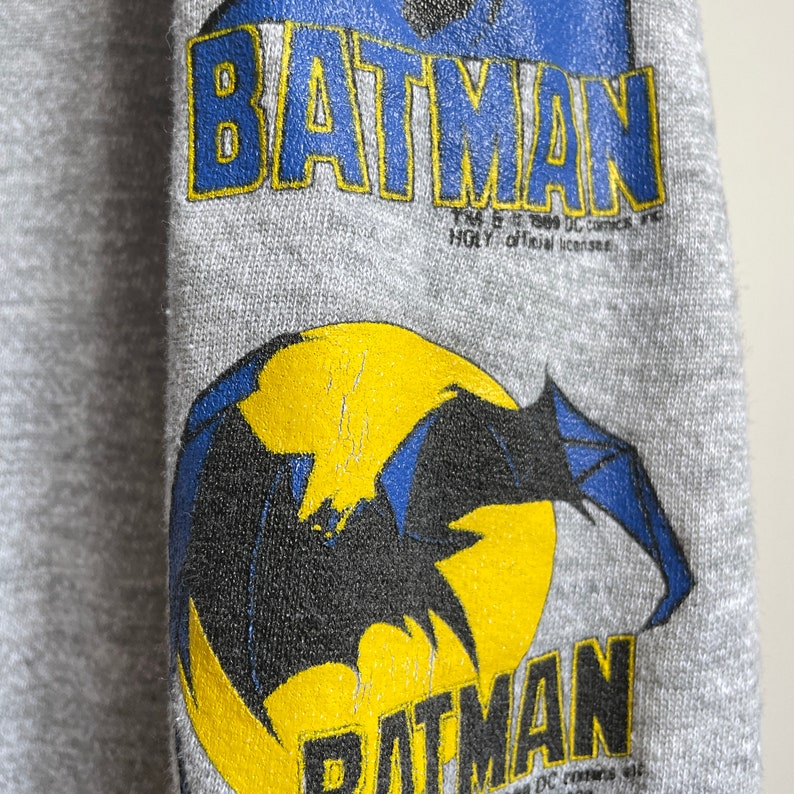 May include: Grey sweatshirt with a black and blue Batman logo and the text "TM & &copy; 1989 DC Comics Inc.  HGL, official licensee."  Below the logo is a yellow circle with a black bat silhouette.