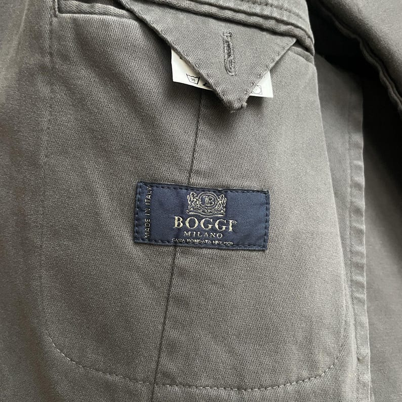 May include: Close-up of the interior of a gray jacket. A navy blue label reads "Boggi Milano" with text below. The jacket's lining is visible, along with a small tag with symbols.