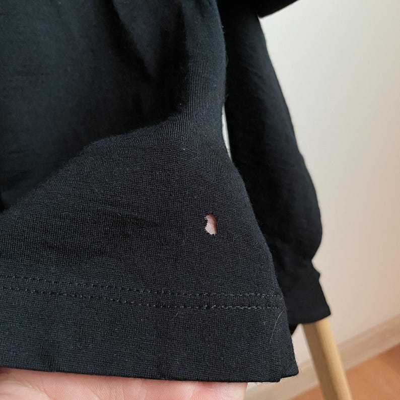 Puede incluir: Camiseta negra de manga larga con un peque&ntilde;o agujero cerca de la parte inferior.