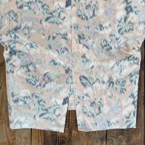 Puede incluir: Una falda con base de color beige y un estampado floral abstracto en tonos azul apagado, verde salvia y rosa suave. La prenda incluye una abertura vertical central en el dobladillo inferior, creando un dise&ntilde;o dividido en la tela.