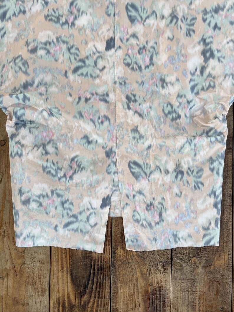 Puede incluir: Una falda con base de color beige y un estampado floral abstracto en tonos azul apagado, verde salvia y rosa suave. La prenda incluye una abertura vertical central en el dobladillo inferior, creando un dise&ntilde;o dividido en la tela.