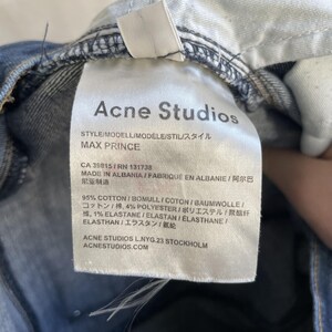 Puede incluir: Primer plano de una etiqueta blanca de vaqueros Acne Studios, con texto negro que detalla el estilo "MAX PRINCE" y la composici&oacute;n de la tela. Los vaqueros son de mezclilla azul.
