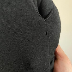 Puede incluir: Tejido de punto negro con escote en V. El tejido tiene una textura sutil y dos peque&ntilde;os agujeros.