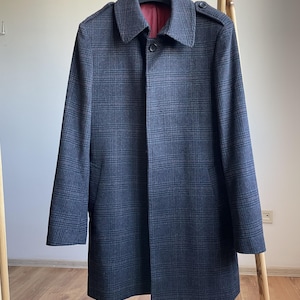 May include: A dark gray plaid coat with a button closure and a collar. The coat is hanging on a wooden rack. The interior lining is a deep red color.