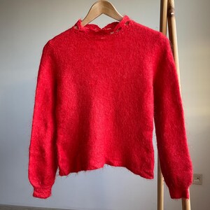 May include: A red fuzzy sweater with a slightly distressed neckline. The sweater has long sleeves and a relaxed fit.
