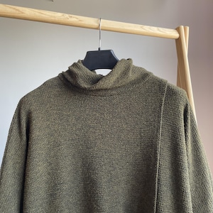 Peut inclure: Pull &agrave; col roul&eacute; vert olive suspendu &agrave; un portant en bois. Le pull pr&eacute;sente un motif en tricot textur&eacute; et un col haut et repli&eacute;. Les manches sont longues et le style est d&eacute;contract&eacute; et confortable.