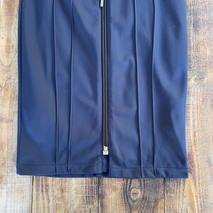 May include: A dark navy blue skirt featuring a central vertical zip closure with a matching pull tab. The garment is constructed with prominent vertical stitched seams that create a panelled appearance throughout the front of the fabric.