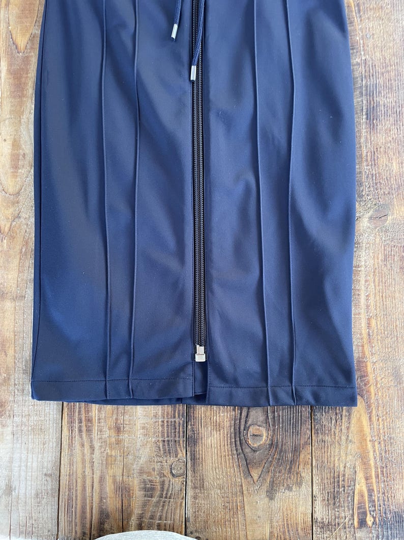 May include: A dark navy blue skirt featuring a central vertical zip closure with a matching pull tab. The garment is constructed with prominent vertical stitched seams that create a panelled appearance throughout the front of the fabric.