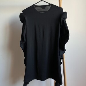Puede incluir: Camiseta negra con un dise&ntilde;o &uacute;nico que presenta mangas grandes y con volantes.