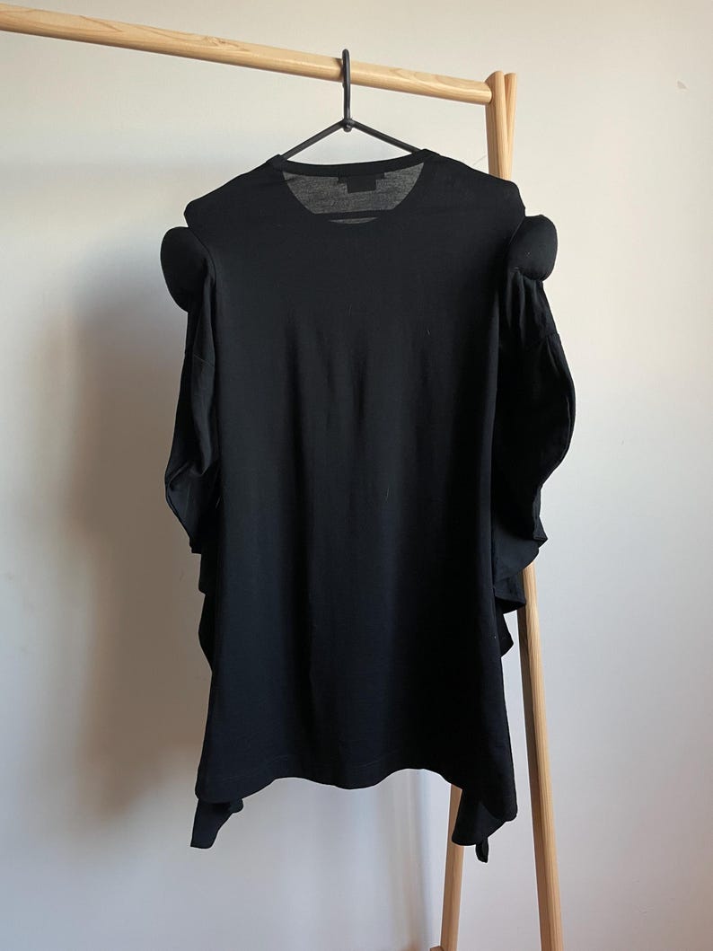 Puede incluir: Camiseta negra con un dise&ntilde;o &uacute;nico que presenta mangas grandes y con volantes.