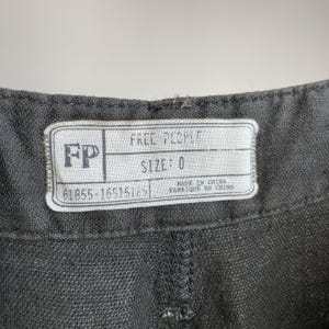 May include: Close-up of a gray garment with a white label. The label reads "FREE PEOPLE" and "SIZE: 0". Below the size is the number "61855-16515125". The label also states "MADE IN CHINA / FABRIQUE EN CHINE".