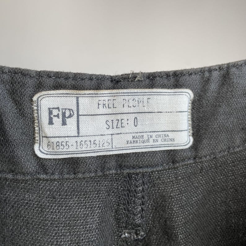 May include: Close-up of a gray garment with a white label. The label reads "FREE PEOPLE" and "SIZE: 0". Below the size is the number "61855-16515125". The label also states "MADE IN CHINA / FABRIQUE EN CHINE".