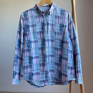 Puede incluir: Camisa de manga larga con estampado de cuadros azules, morados y blancos. La camisa tiene cuello abotonado, bolsillo en el pecho y puños con botones. La marca "Acne" es visible en el cuello.