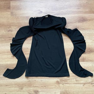 Puede incluir: Un vestido negro de manga larga con cuello redondo y mangas grandes con volantes.