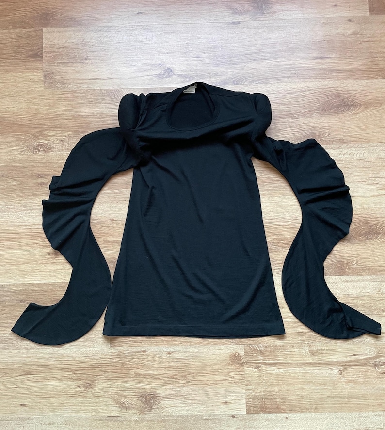 Puede incluir: Un vestido negro de manga larga con cuello redondo y mangas grandes con volantes.