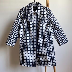 May include: A navy and white geometric print coat with a button-up front and long sleeves. The coat is hanging on a wooden rack. The coat has a collar and two front pockets.
