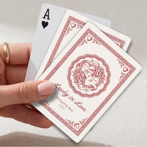 Peut inclure: Un jeu de cartes à jouer avec un motif personnalisé comprenant un emblème de cœur rouge, des roses et le texte Lucky in Love, Michael & Bea, et 11.06.26. Les cartes incluent un as de cœur et un dos décoratif aux bordures rouges.