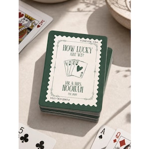 K&ouml;nnte beinhalten: Ein Kartenspiel mit dunkelgr&uuml;nem Rand und cremefarbener Mitte. Das Design zeigt den Text "HOW LUCKY ARE WE?", "MR. & MRS. NOONAN", "EST. 2026" und "FOREVER USA" sowie eine Illustration von vier Spielkarten.