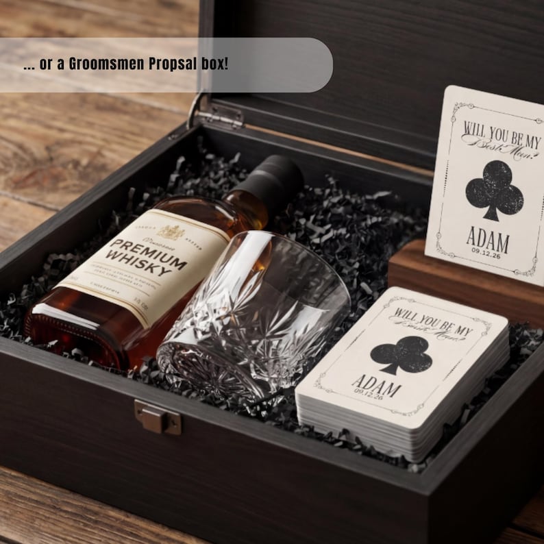 K&ouml;nnte beinhalten: Eine dunkle Holzgeschenkbox mit einer Flasche Premium-Whisky, einem Kristallglas und einem Kartenspiel. Die Karten zeigen ein Kreuz-Symbol und den Text "Will you be my best man? Adam 09.12.26". Der Text auf dem Deckel lautet "... or a Groomsmen Propsal box!"