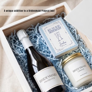 K&ouml;nnte beinhalten: Eine wei&szlig;e Holzgeschenkbox gef&uuml;llt mit hellblauem Papierstreifen, die eine Flasche Bridesmaid Prosecco, eine wei&szlig;e Kerze mit der Aufschrift Bridesmaid Candle White Peony und eine Karte mit der Aufschrift Will You Be My Bridesmaid? und Jordan 09.12.26 enth&auml;lt.