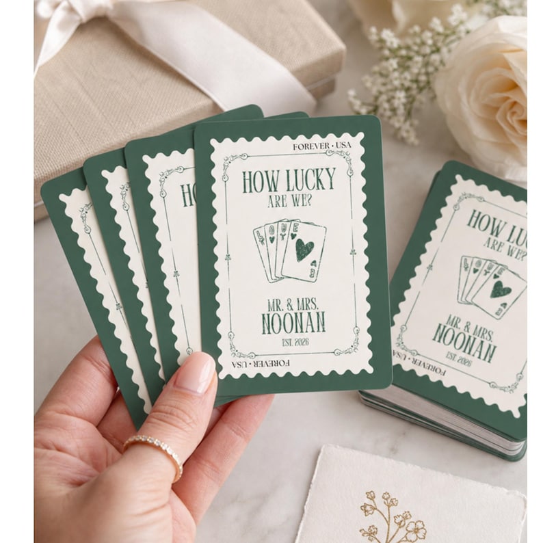 K&ouml;nnte beinhalten: Ein Satz rechteckiger Spielkarten mit dunkelgr&uuml;nem Rand und wei&szlig;er Mitte. Das Design &auml;hnelt einer Briefmarke mit dem Text HOW LUCKY ARE WE?, MR. & MRS. NOONAN, EST. 2026 und FOREVER USA. Eine Grafik mit vier Spielkarten ist mittig platziert.