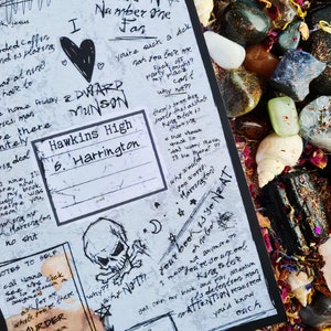 Puede incluir: Una página de diario en blanco y negro con texto escrito a mano y dibujos. El texto incluye las palabras "Corrupted Coffin", "Number One Fan", "Hawkins High", "Harrington", "Edward Munson", "Why Not??", "Good Luck!" y "Your book is so Neat". Los dibujos incluyen un corazón, una calavera y huesos cruzados, y un pentagrama.