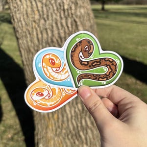 May include: Three heart-shaped stickers featuring cartoon snakes. The snakes are curled up in a heart shape and have different colours and patterns. The stickers are ideal for adding a touch of whimsy to your laptop, water bottle, or planner.