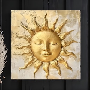 May include: A gold-toned sun with a human face and closed eyes, sculpted in relief on a white canvas. The sun has a textured, slightly rough surface.