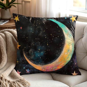 May include: Square throw pillow with a celestial design. The pillow features a crescent moon in shades of teal, orange, and yellow against a dark blue starry background. Gold and pink stars are scattered around the moon.