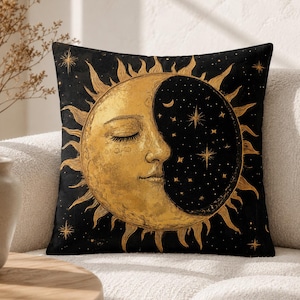 Peut inclure: Un coussin carré avec un fond noir et un grand motif central représentant un soleil et une lune dorés. Le soleil présente un visage humain aux yeux fermés avec des rayons, tandis que la partie lune est noire avec des étoiles dorées.