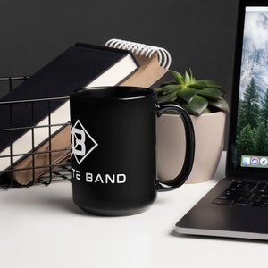 Könnte beinhalten: Schwarze Keramik-Kaffeetasse mit einem weißen Diamantenlogo und dem Text "White Band".