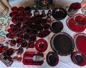 Puede incluir: Una gran colección de vajilla de vidrio prensado rojo rubí que incluye numerosos vasos, cuencos, platos, una jarra, una bandeja de servicio con un servidor de metal y candelabros decorativos, todos con intrincados patrones en relieve.