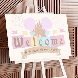 May include: A welcome sign for a baby shower with a pastel pink, blue, and yellow color scheme. The sign features a silhouette of Cinderella's castle with fireworks and the text "Welcome to the Happiest Baby Shower on Earth!"