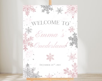 May include: A white welcome sign on a wooden easel, decorated with pink and silver snowflakes. The sign reads "Welcome to Emma's Onerderland" and "December 24th, 2022".