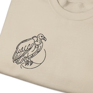 May include: A beige t-shirt with a black line drawing of a vulture on the front.
