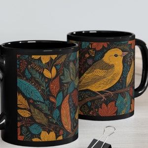 May include: Two black ceramic mugs with a colorful floral and bird design. The mugs feature a yellow bird with brown branches and leaves in shades of blue, green, orange, and red.