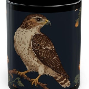 May include: A black coffee mug with a dark blue background featuring a detailed illustration of a brown and white hawk perched on a branch with green leaves and orange flowers.