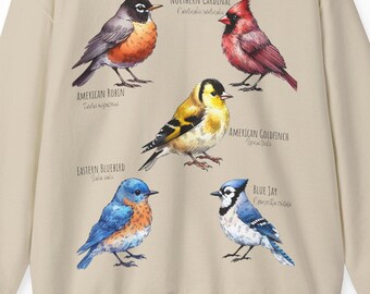 May include: Beige sweatshirt with a graphic print of five different birds. The birds are a Northern Cardinal, American Robin, American Goldfinch, Eastern Bluebird, and Blue Jay. Each bird is labeled with its name and scientific name.